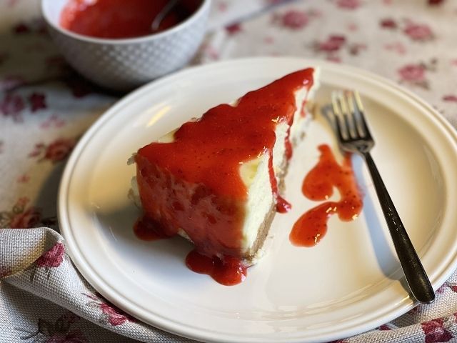 Fetta di New York cheesecake vegana con salsa alle fragole servita nel piatto