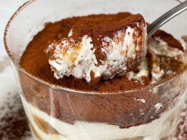 Cucchiaio che affonda in un tiramisù vegano con mascarpone vegetale servito in bicchiere