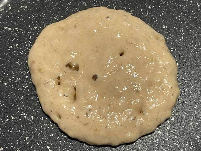 Pancake alla banana senza uova con le bollicine in superficie prima di essere girato.