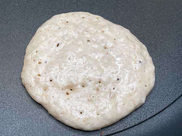 Pancake vegano con le bollicine in superficie, pronto per essere girato durante la cottura.