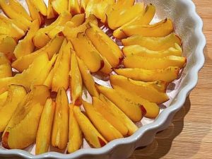 pesche tagliate a fettine disposte nella tortiera per il clafoutis di pesche