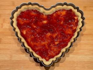 confettura di lamponi stesa sul fondo del guscio di pasta frolla a forma di cuore