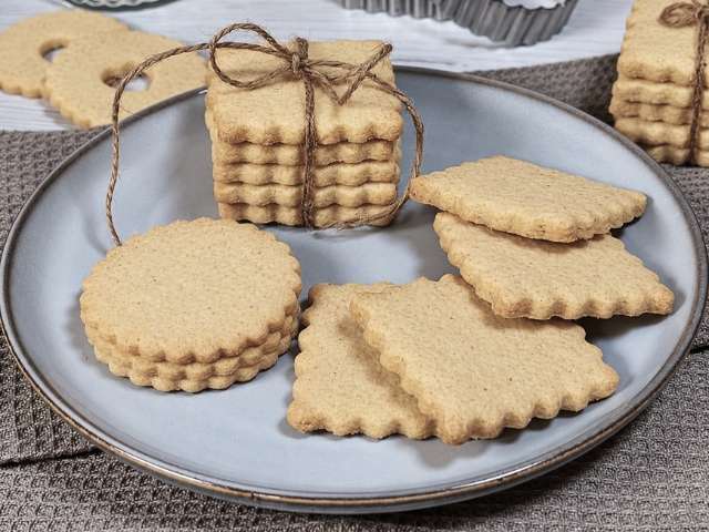 Biscotti di pasta frolla con farina di chufa senza glutine, di diverse forme, disposti su un piatto grigio e legati con spago.