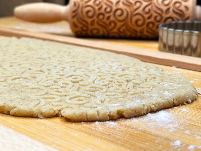 Pasta frolla stesa sul piano di lavoro con un mattarello decorato.