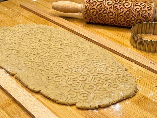 Pasta frolla con farina di chufa senza glutine stesa sul tagliere, con motivi decorativi impressi da un mattarello di legno.