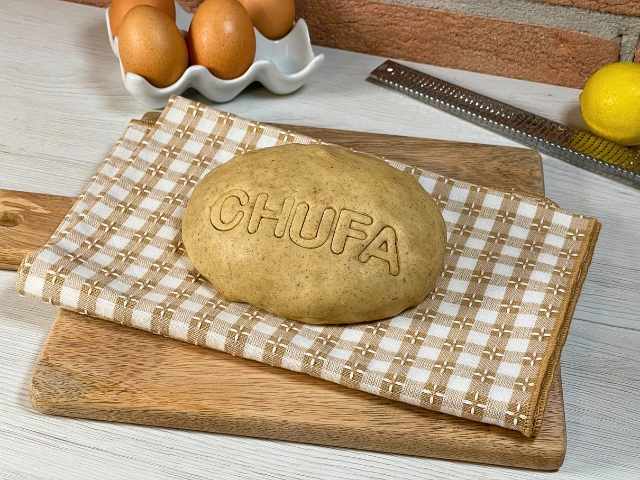 Panetto di pasta frolla con farina di chufa senza glutine, decorato con la scritta CHUFA, con uova e limone sullo sfondo.