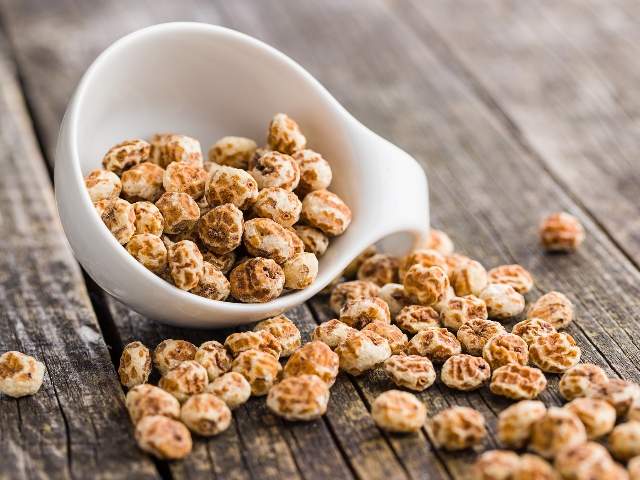 Tuberi di chufa essiccati in una ciotola bianca su un tavolo di legno.